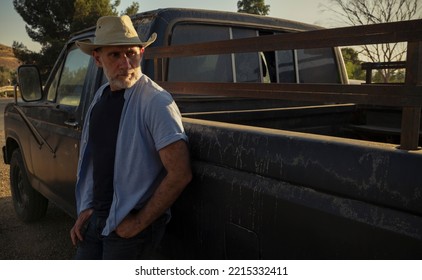 Portrait Of Adult Man In Cowboy Hat Standing Against A Vintage Truck During Sunset