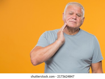 Portrait Of An Adult Man In A Gray T-shirt On A Yellow Background Isolated. An Elderly Man Has A Toothache. Discomfort In The Face Of An Older Man.