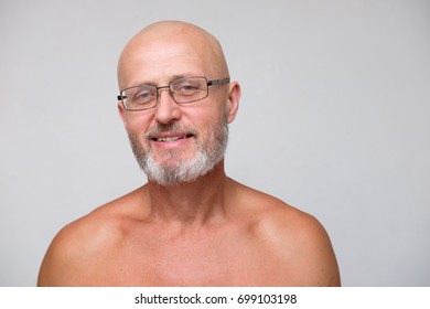 Portrait Of Adult Smiling Bearded Bold Skinhead Grizzled Man In Eyeglasses On Gray