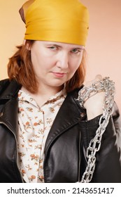 Portrait Of An Adult Stern Woman With A Scarf On Her Head And An Iron Chain In Her Hands