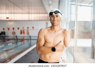 Portrait of an adult swimmer with an amputated arm is posing on a glass of an indoor pool while looking at the camera happily. Concept of disabled swimmers, athletes with an amputated arm. - Powered by Shutterstock