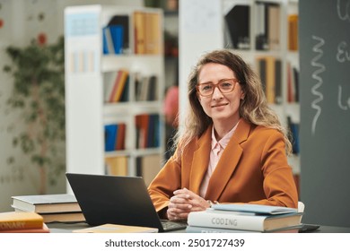 Portrait of adult woman as female teacher sitting at desk and smiling at camera in school library setting