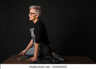 Portrait Of An Adult Woman With Glasses And An Apron On A Black Background