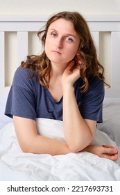 Portrait Of An Adult Woman Sitting On A Bed With A Blanket In A White Bedroom. A Brunette Woman Touches Her Hair And Looks At The Camera, 35 Year Old Female