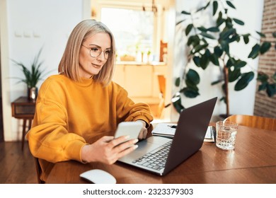 Portrait of adult woman using mobile phone while sitting in living room with laptop  - Powered by Shutterstock