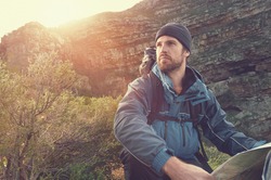 Portrait Of Adventure Man With Map And Extreme Explorer Gear On Mountain With Sunrise Or Sunset