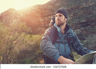 Portrait Of Adventure Man With Map And Extreme Explorer Gear On Mountain With Sunrise Or Sunset