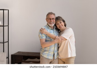 Portrait of affectionate loving old woman cuddling shoulders of sincere mature husband, looking at camera posing in modern living room, feeling excited in own dwelling, retirement lifestyle concept. - Powered by Shutterstock