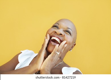 portrait of african 50 years old surprised woman with bald head, smiling on yellow background. Head and shoulders, copy space - Powered by Shutterstock