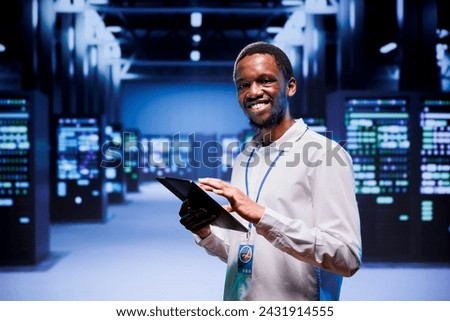 Portrait of african american administrator in front of server clusters in high performance computing data center. Technician monitoring energy consumption across systems, ensuring optimal operations