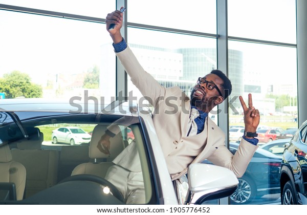 portrait of african\
american car sales consultant in showroom and making selfie photo\
on camera smartphone
