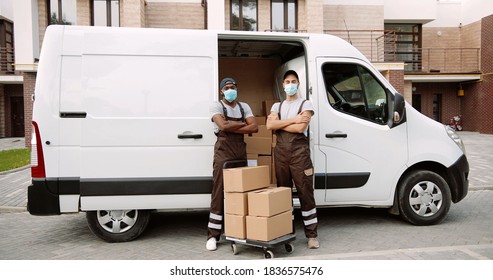 Portrait Of African American And Caucasian Delivery Men In Mask And Uniform In Front Of His Van. 