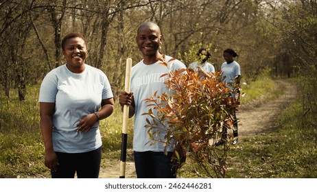 Portrait of african american couple fighting to preserve natural environment by planting trees, collecting rubbish and cultivating consciousness. Volunteers save the planet. Camera B. - Powered by Shutterstock