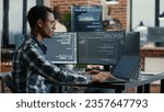 Portrait of african american developer using laptop to write code sitting at desk with multiple screens parsing algorithm in software agency. Coder working on user interface using portable computer.