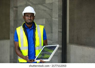 Portrait Of African American Electrician Engineer In Safety Helmet And Uniform Are Checking Solar Panels Condition.