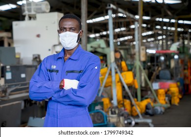 Portrait of African American engineer worker wearing surgical mask with arms crossed in factory on a business day. New normal, epidemic prevention. Concept of Industrial manufacturing.
