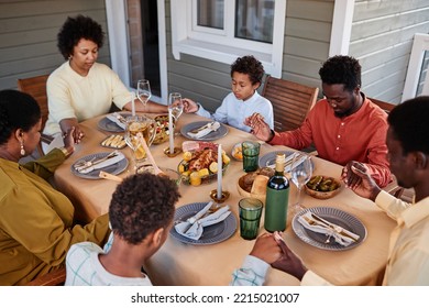 Portrait of African American family saying grace at dinner table and holding hands in cozy evening setting - Powered by Shutterstock