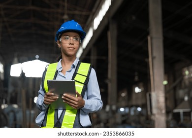 Portrait African American female engineer with tablet working in heavy metal industrial factory. Confident technician woman wearing vest and helmet safety standing at the manufacturing plant. - Powered by Shutterstock