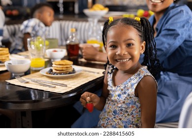 Portrait of african american girl holding strawberry while having breakfast with family at home. Unaltered, family, togetherness, childhood, food, fresh, dining table and lifestyle concept. - Powered by Shutterstock