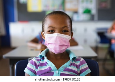 Portrait Of African American Girl Wearing Face Mask Sitting On Her Desk In The Class At School. Education Back To School Health Safety During Covid19 Coronavirus Pandemic