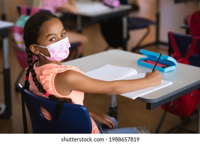 Portrait Of African American Girl Wearing Face Mask Sitting On Her Desk In The Class At School. Education Back To School Health Safety During Covid19 Coronavirus Pandemic