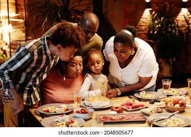 Portrait Of African- American Grandma Blowing Candles While Celebrating Birthday With Family In Cozy Setting