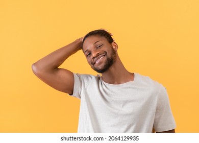 Portrait Of African American Guy Smiling At Camera And Touching Hair With Hand, Posing Over Yellow Studio Background. Handsome Young Black Man Showing Positive Emotion