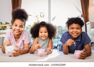 Portrait Of African American Kids Saving Money In A Piggy Bank In Living Room At Home