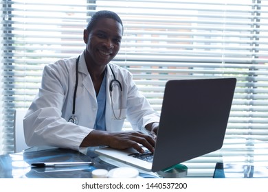 Portrait Of African American Male Doctor Using Laptop While Looking At Camera At Desk In The Hospital