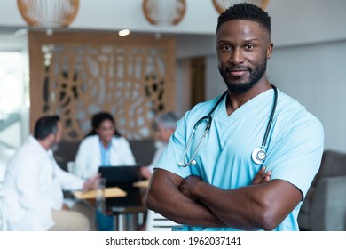 Portrait of african american male doctor smiling, with colleagues in discussion in the background. medicine, health and healthcare services. - Powered by Shutterstock