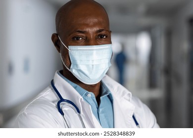 Portrait of african american male doctor wearing lab coat and face mask in corridor at hospital. Hospital, hygiene, medicine, healthcare and work, unaltered. - Powered by Shutterstock