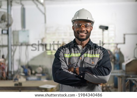 Portrait of African American male engineer in uniform smiling and standing cross arm in industrial factory
