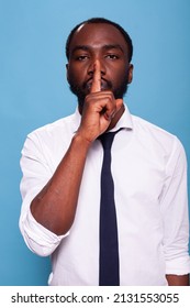 Portrait Of African American Man Doing Hush Sign With Index Finger Over Lips On Blue Background. Calm Businessman Asking For Silence Doing Shush Hand Gesture.