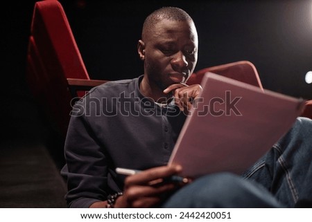 Portrait of African American man reading script in theater and rehearsing for performance
