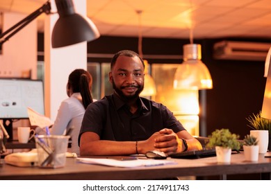 Portrait Of African American Man Working On Computer At Desk During Sunset, Using Data Network. Creating Business Presentation With Research And Information To Do Report In Office With Big Windows.