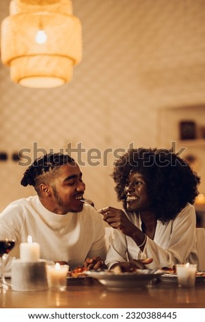 Portrait of an african american married couple having dinner by candlelight at home. Black romantic couple celebrating anniversary or a Valentines day. Woman is feeding her boyfriend or husband.