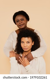 Portrait Of African American Middle Aged Mother And Adult Daughter Hugging And Holding Hands Isolated On Beige