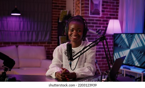 Portrait Of African American Podcaster Sitting At Desk In Home Recording Studio With Boom Arm Microphone And Digital Audio Mixer. Online Radio Host Smiling Confident At Camera While Broadcasting Live.