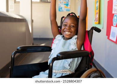 Portrait of african american schoolgirl sitting in wheelchair and raising hands at elementary school. Disability, education, childhood, development, learning and school, unaltered. - Powered by Shutterstock