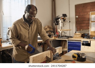 Portrait of African American senior man cutting wood while building furniture in sunlit workshop - Powered by Shutterstock