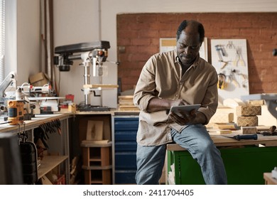 Portrait of African American senior man using digital tablet in small business carpentry workshop - Powered by Shutterstock