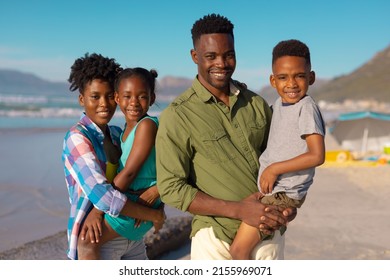 Portrait Of African American Smiling Young Parents Carrying Son And Daughter At Beach Against Sky. Nature, Summer, Unaltered, Beach, Childhood, Family, Togetherness, Lifestyle, Enjoyment, Holiday.