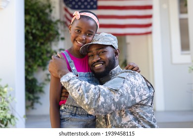 Portrait Of African American Soldier Father Hugging Smiling Daughter In Front Of House. Soldier Returning Home.