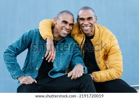 Portrait of African American twin brothers smiling and embracing each other, wearing blue and yellow trendy clothes
