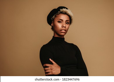 Portrait of african american woman in cap against brown background. Fashion woman standing with arms crossed. - Powered by Shutterstock