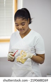 Portrait Of African American Woman Dentist In White Coat With Toothbrush And Plastic Jaw