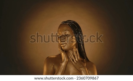 Portrait of an African American woman with golden skin in a studio on a brown background with circular light. A woman touches her metal skin. Fashion, art, design, cosmetology.