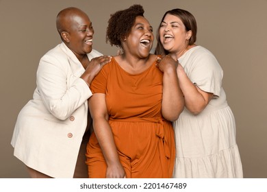 Portrait Of An African American Woman In Her 30's, A Black Woman In Her 50's, And A Middle Eastern Woman In Her 40's Laughing Together On A Neutral Background.