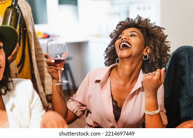 Portrait of an African American woman laughing with open mouth drinking wine sitting with her friends dining at multiethnic party - people lifestyle concept - Powered by Shutterstock