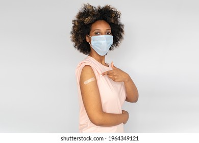 Portrait Of African American Woman Showing Her Arm With Band Aid After Coronavirus Covid-19 Vaccine Injection, Wearing Medical Mask